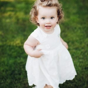 Top view of happy cute toddler girl with curly hair standing in the garden and looking at the camera